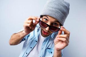 salut là vue de dessus d'un jeune homme drôle ajustant ses lunettes de soleil et regardant la caméra en se tenant debout sur fond gris photo