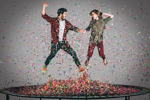 plaisir du trampoline. tir en l'air d'un beau jeune couple joyeux se tenant la main tout en sautant sur un trampoline avec des confettis tout autour d'eux photo