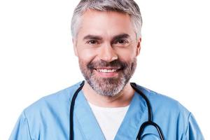 chirurgien confiant. portrait d'un chirurgien mature heureux en uniforme bleu regardant la caméra et souriant tout en se tenant isolé sur blanc photo