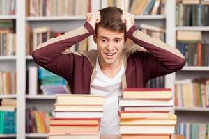 tant de travail devant un jeune homme fatigué tenant sa tête dans les mains et regardant les piles de livres tout en étant assis au bureau de la bibliothèque photo