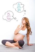 garçon ou fille femme enceinte réfléchie levant les yeux et tenant la main sur le menton tout en étant assis sur fond blanc photo