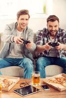 nous aimons ce jeu deux jeunes hommes joyeux jouant à des jeux vidéo assis sur un canapé photo