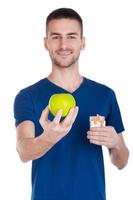 faire un bon choix jeune homme confiant tendant la main avec une pomme dedans tout en tenant un paquet de cigarettes dans un autre et isolé sur fond blanc photo