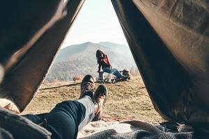 réveillé à l'endroit idéal. jeune homme méconnaissable profitant de la vue sur la chaîne de montagnes depuis la tente pendant que sa petite amie se repose près du feu de camp photo