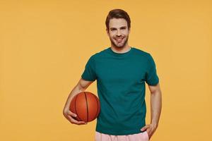 beau jeune homme tenant un ballon de basket et souriant en se tenant debout sur fond jaune photo