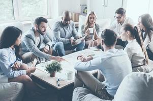 discuter de stratégie. groupe de gens d'affaires confiants discutant de quelque chose assis autour du bureau ensemble et pointant un grand papier posé dessus photo