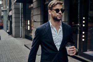 parfait homme d'affaires. beau jeune homme en tenue décontractée intelligente portant une tasse jetable en marchant dans la rue de la ville photo