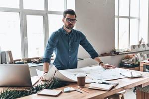 professionnel à succès. beau jeune homme utilisant un plan tout en travaillant dans l'espace de travail créatif photo