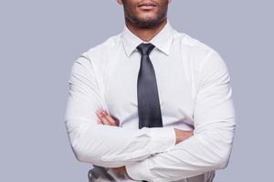 homme d'affaires confiant. image recadrée d'un jeune homme africain sérieux en chemise et cravate en gardant les bras croisés en se tenant debout sur fond gris photo