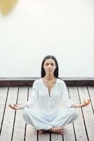 femme médiatrice. belle jeune femme en vêtements blancs assise en position du lotus et gardant les yeux fermés tout en méditant à l'extérieur photo