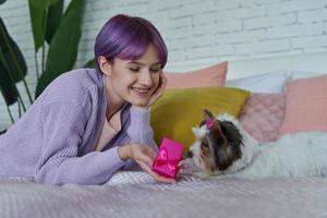 heureuse jeune femme tenant une petite boîte cadeau en position couchée dans son lit avec son chien photo