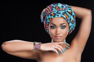 beauté traditionnelle. belle femme africaine en foulard et bijoux posant sur fond noir et regardant la caméra photo