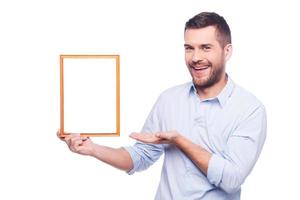 copier l'espace dans le cadre de l'image. beau jeune homme en chemise tenant un cadre photo et le pointant avec le sourire en se tenant debout sur fond blanc