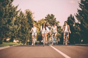 faire du vélo avec plaisir. groupe de jeunes faisant du vélo le long d'une route et ayant l'air heureux photo