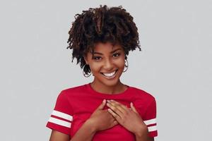 séduisante jeune femme africaine regardant la caméra et souriant en se tenant debout sur fond gris photo