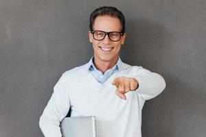 toujours prêt à vous aider. joyeux homme mûr portant un ordinateur portable et vous pointant en se tenant debout sur fond gris photo