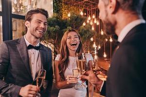 groupe de personnes en tenues de soirée communiquant et souriant tout en passant du temps à une fête de luxe photo