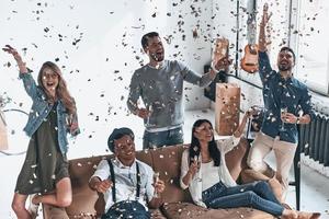 que la fête commence. vue de dessus de jeunes gens heureux en tenue décontractée buvant du champagne tout en faisant la fête avec des confettis volant partout photo