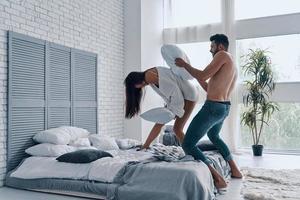 amants et amis. toute la longueur d'un jeune couple heureux ayant une bataille d'oreillers amusante tout en passant du temps sans soucis dans la chambre photo