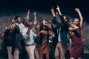 profiter d'une fête incroyable. groupe de beaux jeunes gens dansant avec des flûtes à champagne et ayant l'air heureux photo