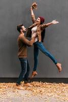 amusement d'automne. beau jeune couple s'amusant ensemble en se tenant debout contre un mur gris avec des feuilles mortes orange autour d'eux photo