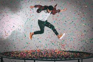 plaisir coloré. tir en l'air d'un beau jeune homme sautant sur un trampoline avec des confettis tout autour de lui photo