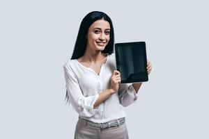 toujours là pour m'aider jolie jeune femme en chemise blanche tenant une tablette numérique et souriant debout sur fond gris photo