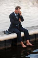 Encore raté. homme d'affaires mature déprimé touchant son visage avec la main alors qu'il était assis pieds nus sur le quai photo