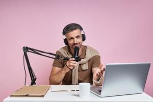 bel homme dans un casque à l'aide d'un microphone lors de l'enregistrement d'un podcast sur fond rose photo