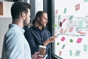 planifier la prochaine étape. deux jeunes collègues en tenue décontractée intelligente utilisant des notes adhésives sur la fenêtre tout en travaillant ensemble au bureau photo