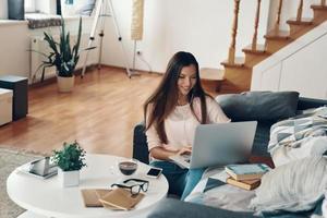 belle jeune femme en tenue décontractée utilisant un ordinateur portable tout en se reposant à la maison photo