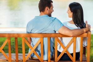 un rendez-vous romantique. vue arrière du beau jeune couple aimant assis sur le banc ensemble et souriant les uns aux autres photo