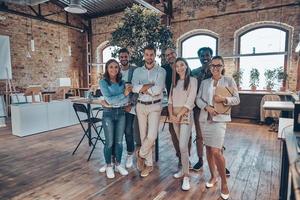 toute la longueur des jeunes gens modernes en vêtements décontractés intelligents regardant la caméra et souriant tout en se tenant au bureau photo