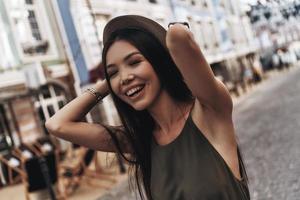 tenue cool. jolie jeune femme gardant les yeux fermés et souriant tout en se tenant à l'extérieur photo