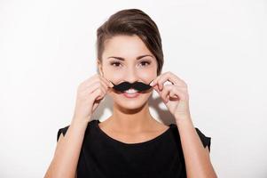 simplement s'amuser. belle jeune femme aux cheveux courts tenant une fausse moustache sur son visage et souriant photo