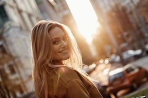 beauté coquette. jolie jeune femme regardant la caméra et souriant tout en se tenant à l'extérieur photo