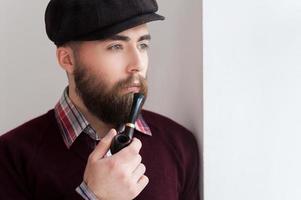 fumer la pipe. portrait de beau jeune homme au chapeau fumant une pipe et regardant loin photo