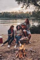 Meilleurs amis du monde. groupe de jeunes en tenue décontractée souriant tout en profitant d'une fête sur la plage près du feu de camp photo