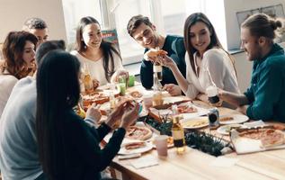 fête inoubliable. groupe de jeunes en tenue décontractée mangeant de la pizza et souriant tout en dînant à l'intérieur photo