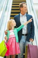 père et fille faisant du shopping. joyeux père et fille descendant par un escalator et tenant des sacs à provisions photo