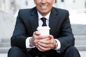 se détendre avec une tasse de café. image recadrée d'un homme mûr joyeux en tenues de soirée tenant une tasse de café et souriant tout en étant assis à l'extérieur de l'escalier photo