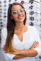 j'ai fait mon choix. belle jeune femme à lunettes de soleil en gardant les bras croisés et souriant tout en se tenant dans un magasin d'optique photo