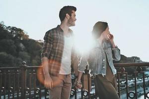 match parfait. Beau jeune couple main dans la main et en détournant les yeux tout en se tenant sur le pont à l'extérieur photo