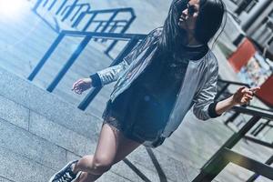 la beauté en déplacement. belle jeune femme en tenue décontractée regardant loin tout en courant dans les escaliers à l'extérieur photo