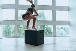 faire des efforts. jeune femme moderne en vêtements de sport sautant pendant l'exercice dans la salle de gym photo