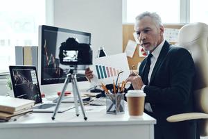 homme senior en costume d'affaires élégant montrant un graphique tout en faisant une vidéo sur les réseaux sociaux photo