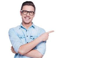 joyeux jeune homme pointant vers l'espace de copie. beau jeune homme en chemise regardant la caméra et pointant vers l'extérieur en se tenant debout sur fond blanc photo