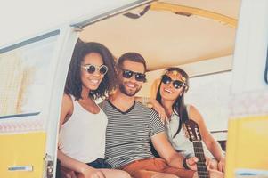 profiter de l'été avec des amis. deux jeunes femmes et un homme se lient les uns aux autres et sourient assis ensemble à l'intérieur de la camionnette rétro photo