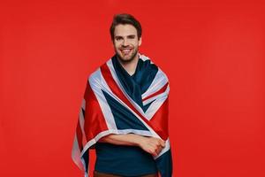 beau jeune homme en tenue décontractée portant le drapeau britannique sur les épaules et souriant photo