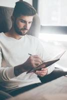 prendre des notes. jeune homme confiant écrivant quelque chose dans un cahier tout en étant assis à son lieu de travail au bureau photo